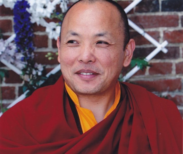 Khenpo Trinley Gyaltsen souriant devant un mur en brique